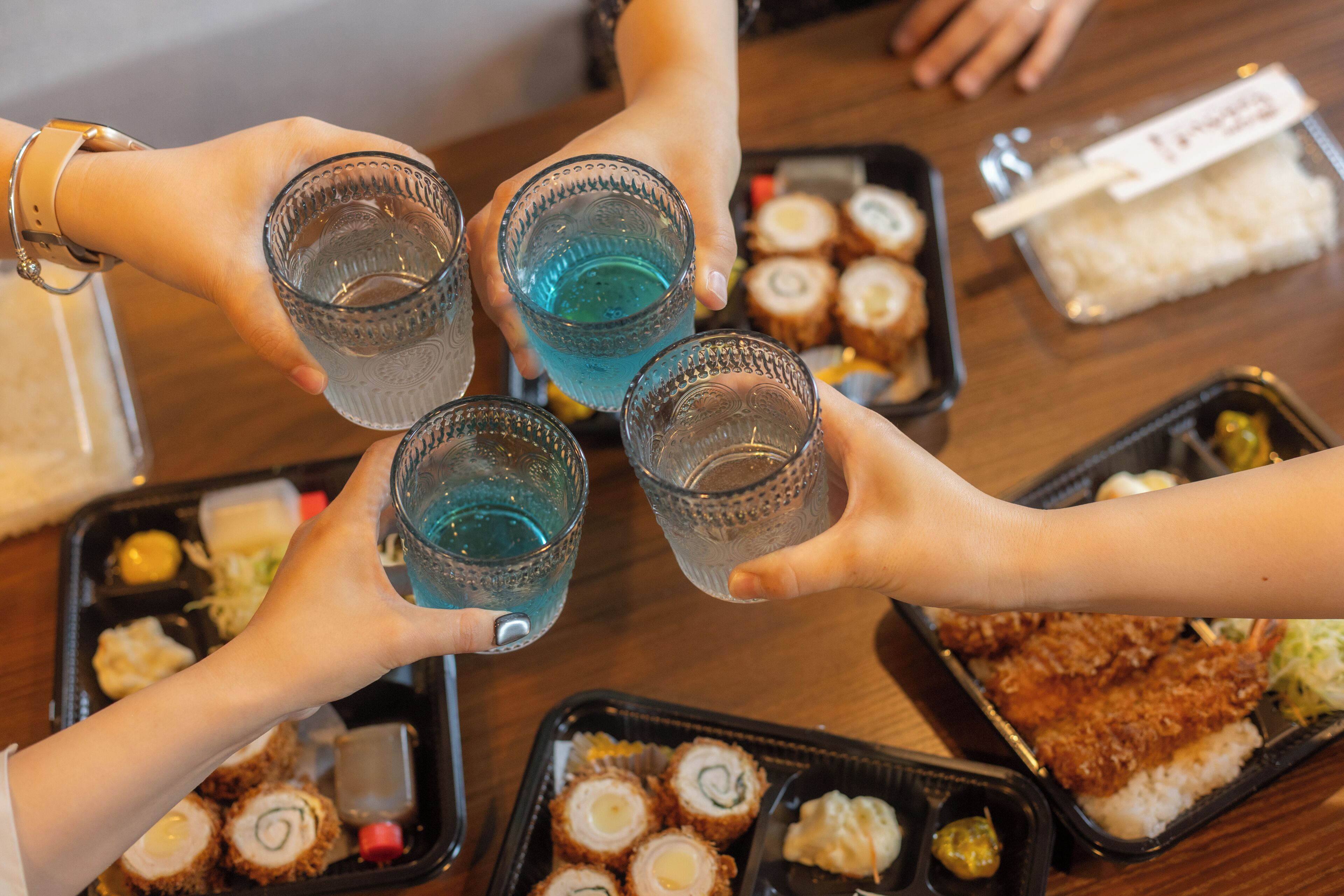 A group of people holding glasses of blue drink, seated around a table with food and drink containers.