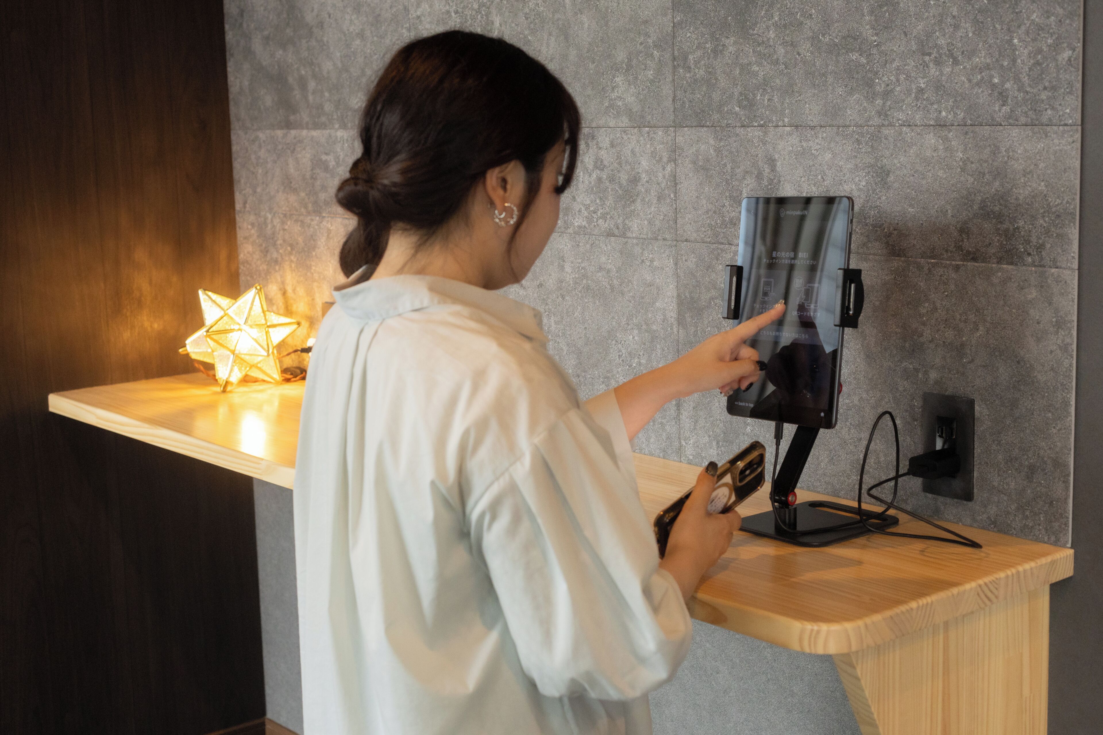 A person using a smartphone at a wooden counter with a modern light fixture in the background.