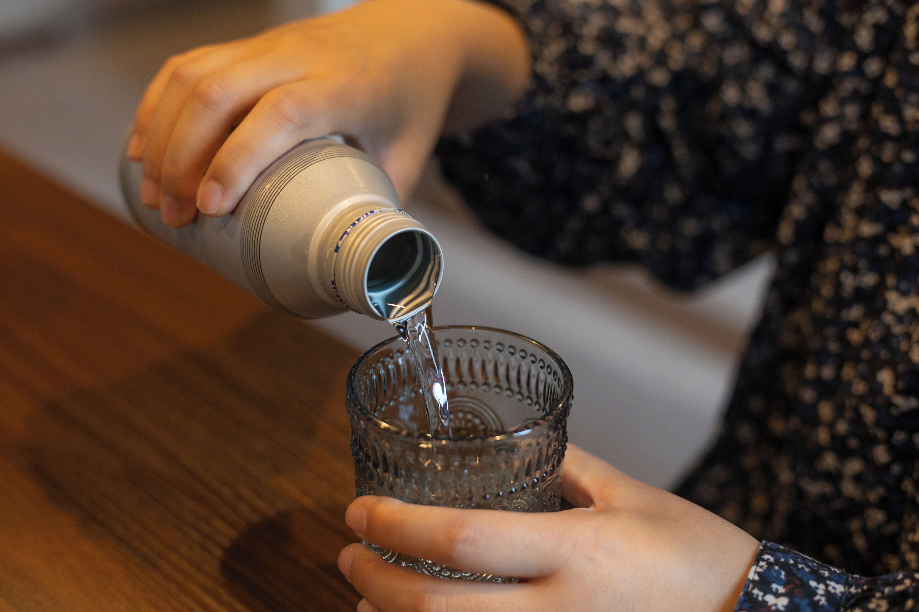 Iemand giet een heldere vloeistof uit een fles in een glas.