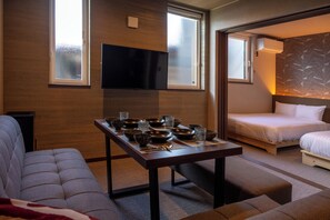 A hotel room with a sofa, a dining table set with bowls and glasses, a bed, and a TV mounted on the wall. - hoshinohikarinoyado Biei (Biei)