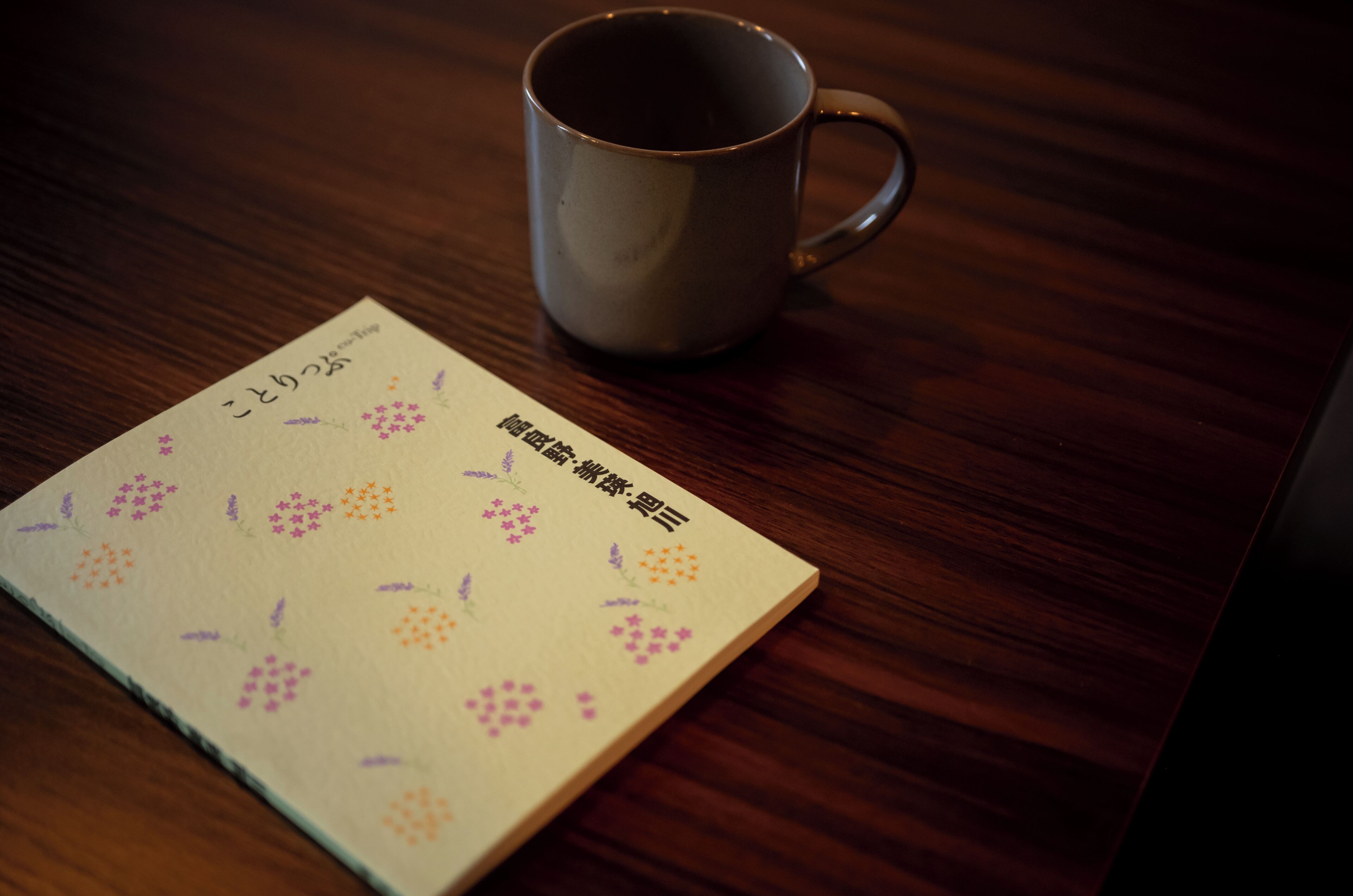 A wooden table with a ceramic mug and a notebook with floral patterns.