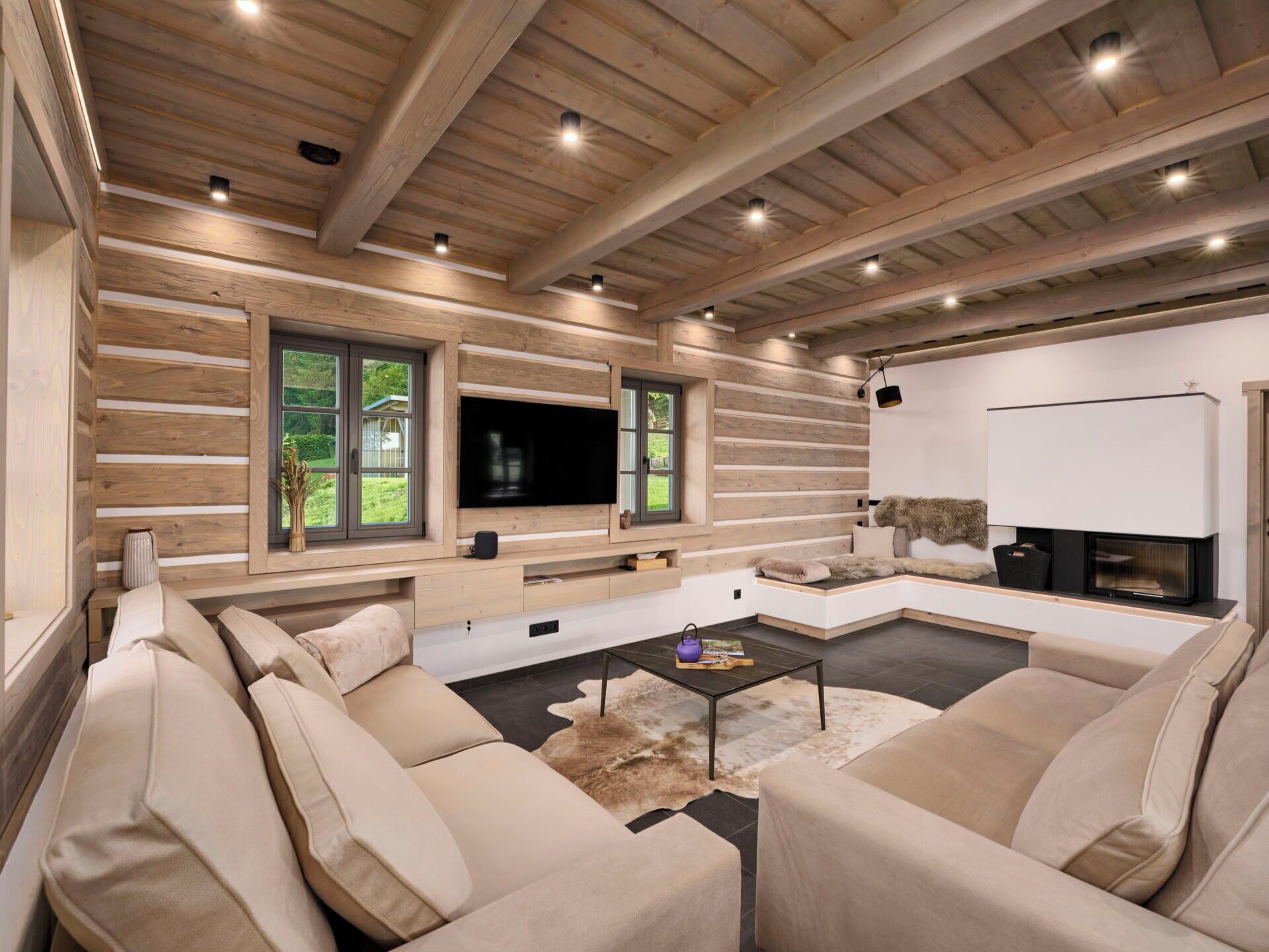 A modern living room with a large TV, wooden beams, and a fireplace.