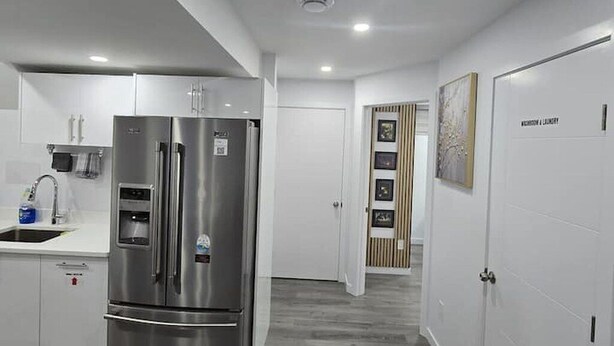 Eine moderne Küche mit einem Edelstahl-Kühlschrank, weißen Schränken und einer Holztür mit gerahmten Bildern.