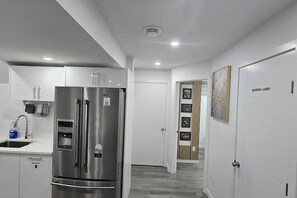 A modern kitchen with a stainless steel refrigerator, white cabinetry, and a wooden door with framed pictures. - Davigo Luxe.
Luxuriously furnished with guaranteed guests' privacy & comfort. (Winnipeg)