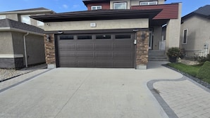 Eine Garage mit einer Hausnummer 33 über der Tür, einer Auffahrt, die zur Garage führt, und einer Steinwand links.