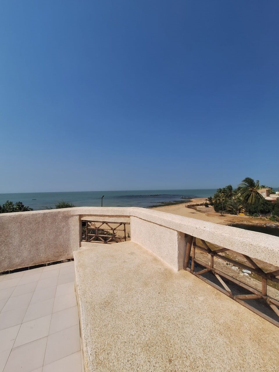 A balcony with a view of the sea, a tiled floor, and a concrete wall.
