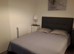 Ein Schlafzimmer mit Bett, Nachttisch, Lampe, Heizkörper und Wandbild.