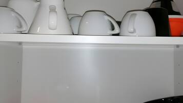 Una cocina con distintos utensilios, incluyendo ollas, sartenes y tazas, ordenados en estantes.
