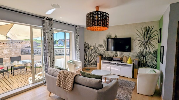 Ein modernes Wohnzimmer mit Sofa, Couchtisch, Fernseher und einem Balkon mit Gartenmöbeln.