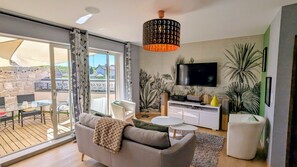 Una sala de estar moderna con sofá, mesa de centro, televisor y un balcón con mobiliario exterior.