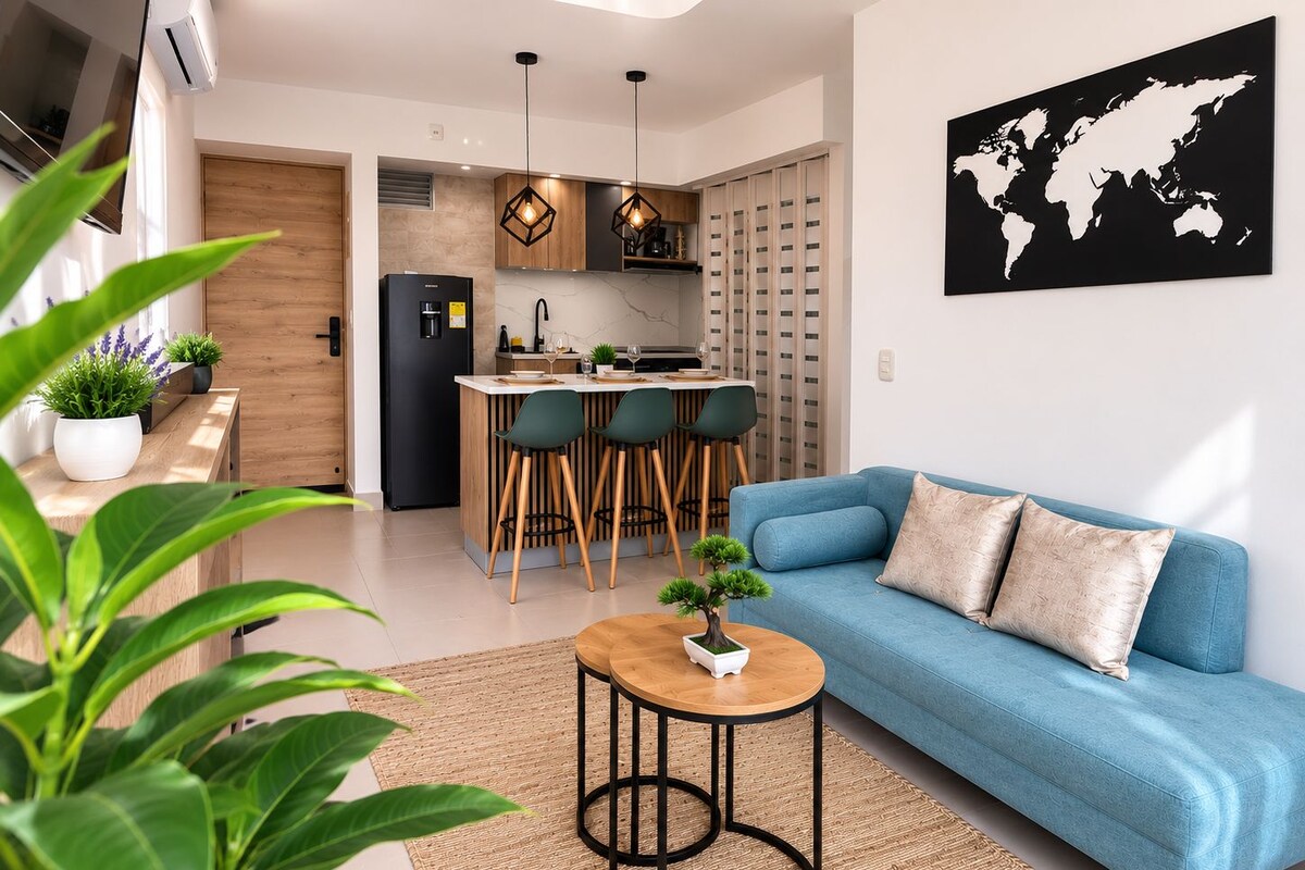 Una sala de estar moderna con un sofá azul, una pequeña mesa redonda y una zona de cocina con un juego de comedor.