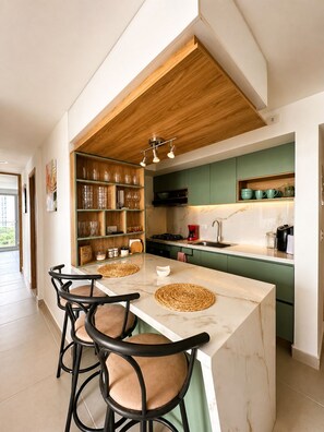 A modern kitchen with a marble island, green cabinets, and a wooden ceiling. - MG Design & Stays (Cartagena de Indias)