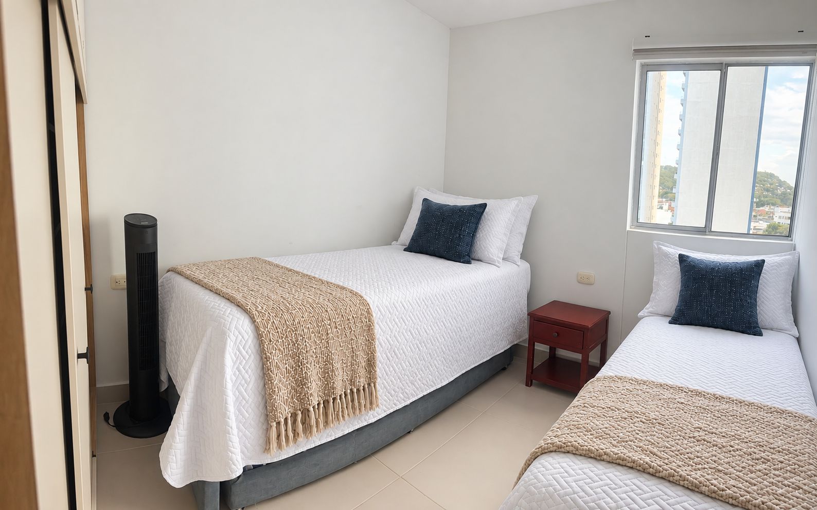 Una habitación con dos camas, una mesita de noche pequeña, un calentador y una ventana.