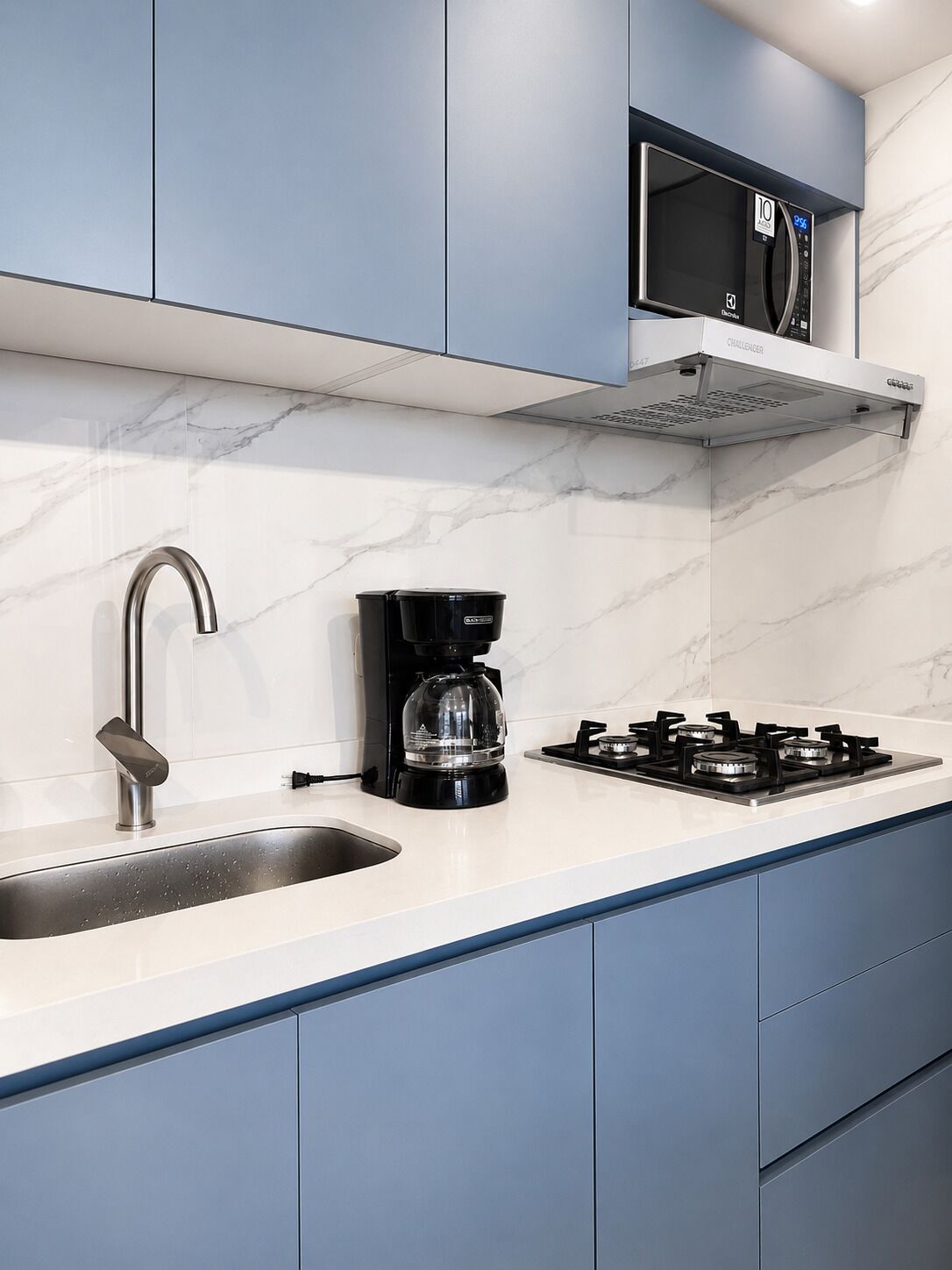 A modern kitchen with a stainless steel sink, a coffee maker, a gas stove, and a microwave on a marble countertop.