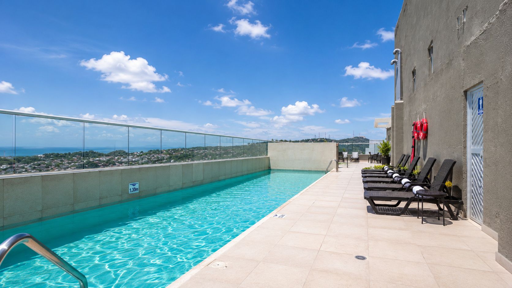 A rooftop pool with clear blue water, a glass balustrade, and lounge chairs.
