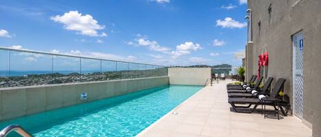 A rooftop pool with clear blue water, a glass balustrade, and lounge chairs.