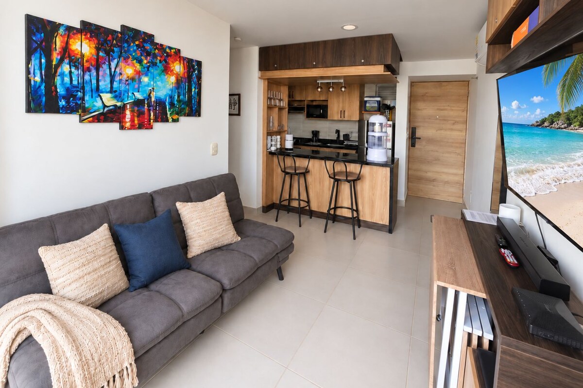 Una sala de estar moderna con un sofá gris, una mesa de centro y una pantalla de televisión mostrando una vista de playa.