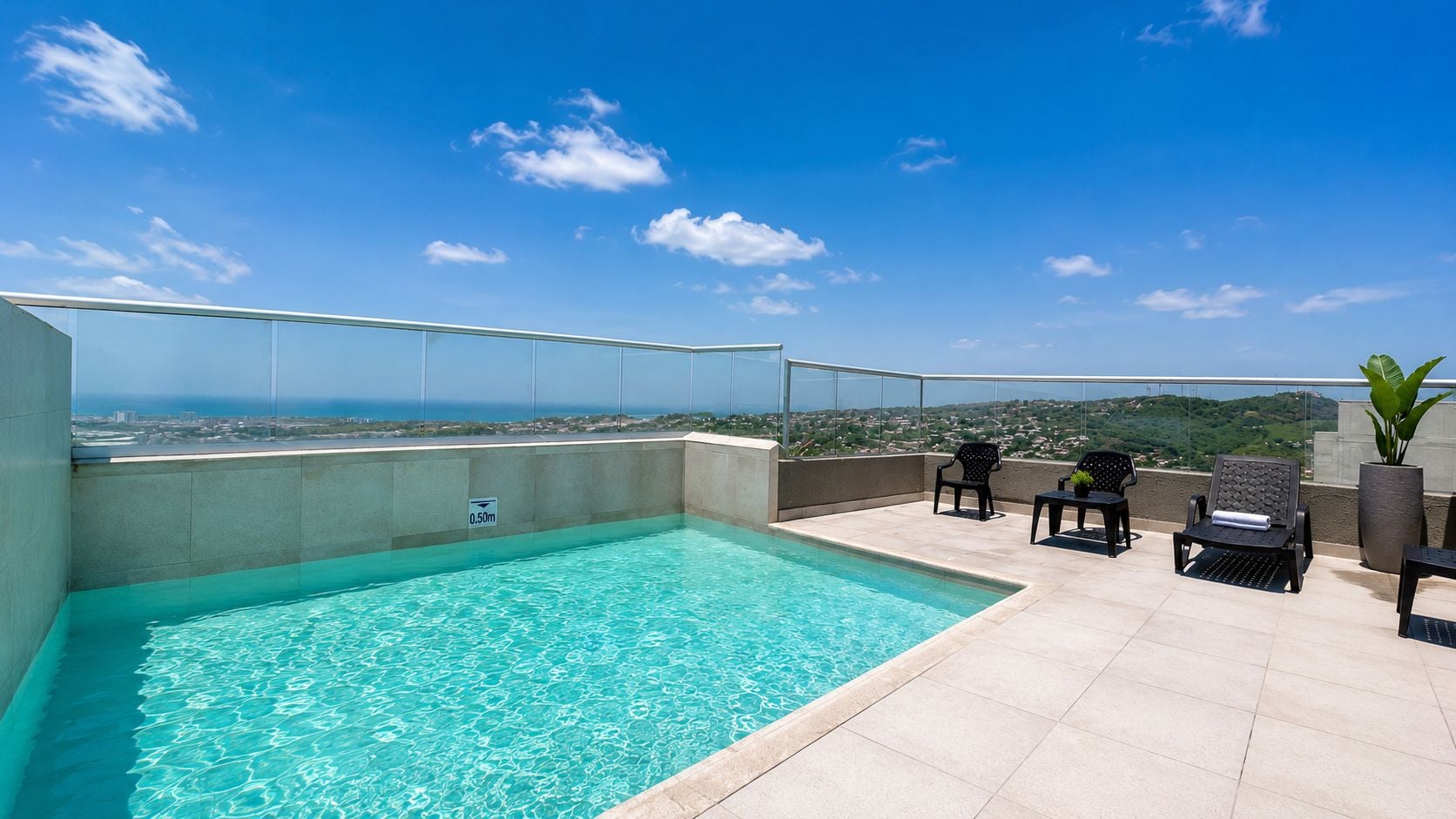 A rooftop swimming pool with clear blue water, surrounded by tiled flooring and black lounge chairs.