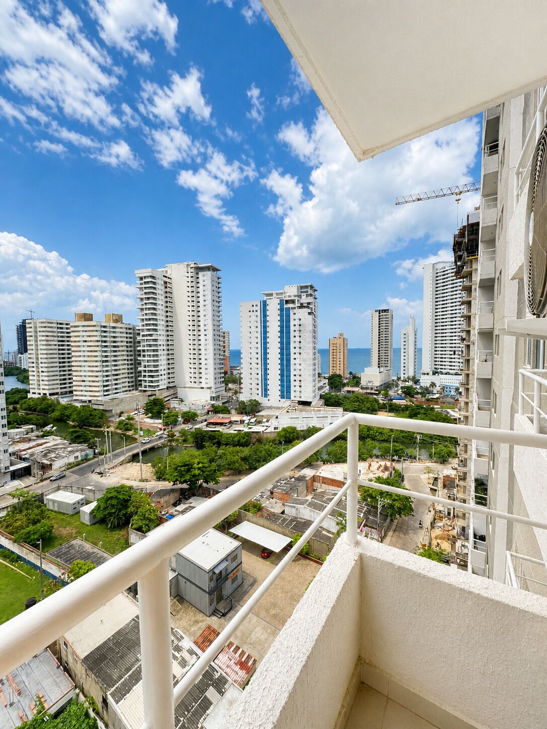 A high-rise building with multiple balconies, a clear sky, and a view of other buildings and greenery below.