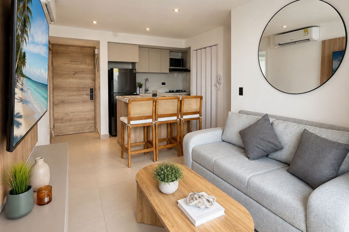 Una sala de estar moderna con un sofá gris, una mesa de centro de madera con una planta y un televisor montado en la pared.