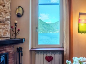 Ein Zimmer mit Steinsturz, einem Fenster mit Seeblick und Hügeln, einem Kamin mit herzförmiger Dekoration und einem wandmontierten Kandelaber.