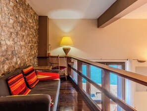 Ein Balkon mit Holzbalkon, einer Steinmauer, einer Couch mit gestreiften Kissen und einer Lampe.
