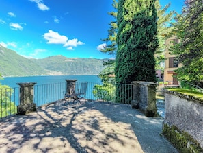 A terrace with a view of a lake, stone pillars, and a chair. - Beautiful apartment for 4 people with WIFI, pool, TV, terrace and panoramic view (Nesso)