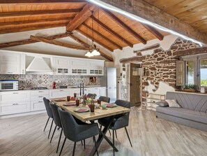 Une cuisine spacieuse avec des meubles blancs, une table à manger en bois et un mur en pierre.