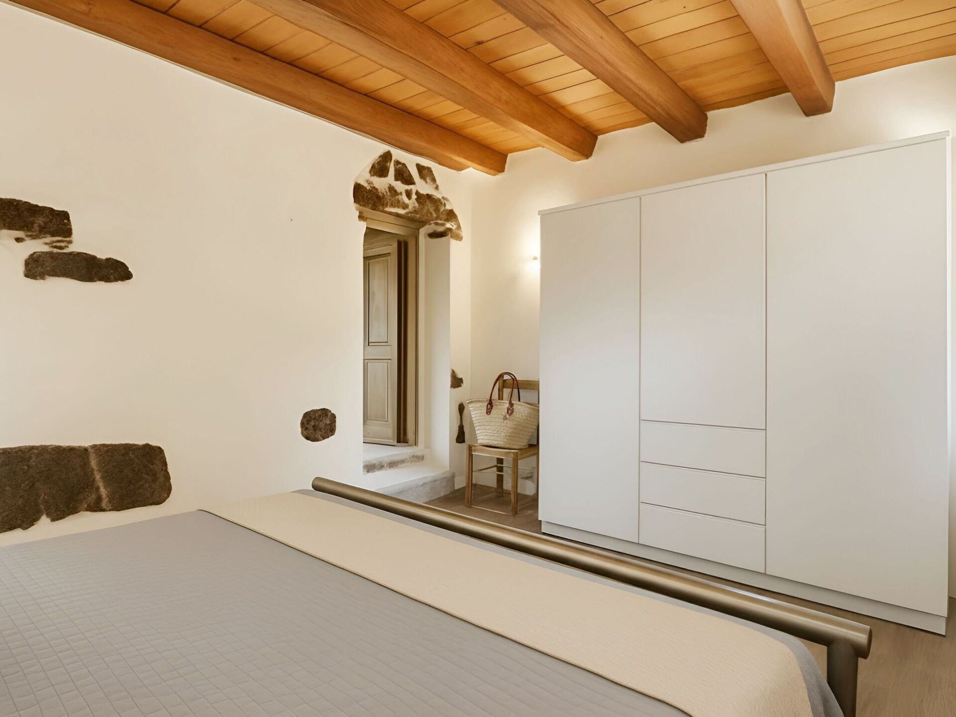 Un dormitorio con cama, armario, silla y techo de madera.