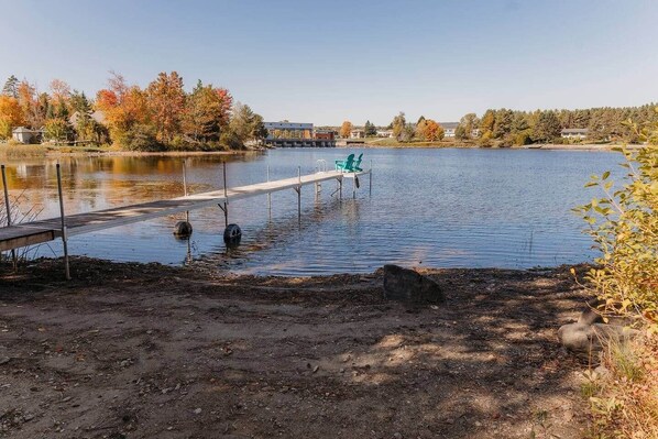 Un lago con un muelle, una silla y un edificio al fondo.