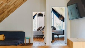 Une pièce de style « loft » avec un plafond en pente, un canapé de couleur sombre, une petite table et un lit doté d’une tête de lit.