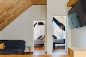 A loft-style room with a sloped ceiling, a dark-colored sofa, a small table, and a bed with a headboard.