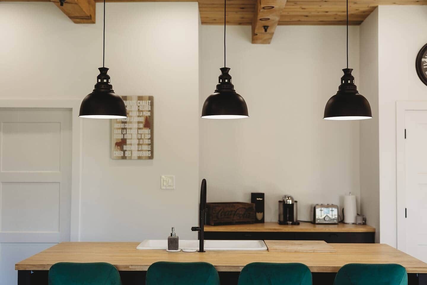 Un espace repas avec une table en bois, trois lampes suspendues noires et des chaises vertes.