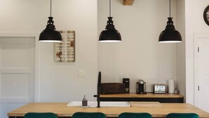 Un espace repas avec une table en bois, trois lampes suspendues noires et des chaises vertes.
