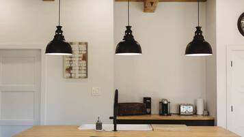 Un espace repas avec une table en bois, trois lampes suspendues noires et des chaises vertes.