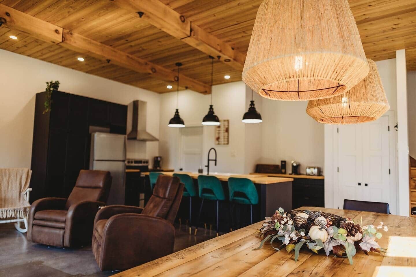 Une cuisine moderne avec des poutres en bois au plafond, un coin repas avec des chaises en cuir et une table en bois agrémentée d'un élément décoratif central.
