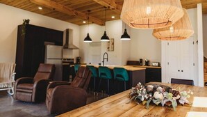 Une cuisine moderne avec des poutres en bois au plafond, un coin repas avec des chaises en cuir et une table en bois agrémentée d'un élément décoratif central.