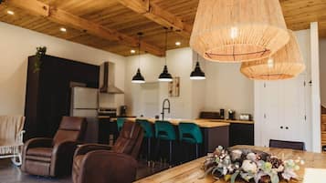 Une cuisine moderne avec des poutres en bois au plafond, un coin repas avec des chaises en cuir et une table en bois agrémentée d'un élément décoratif central.