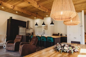 A modern kitchen with wooden ceiling beams, a dining area with leather chairs, and a wooden table with a centerpiece.
