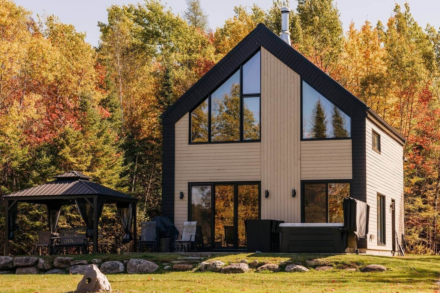 Une maison moderne à deux étages, dotée de grandes fenêtres, d’un patio couvert et d’un chemin en pierre.