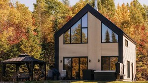 Une maison moderne à deux étages, dotée de grandes fenêtres, d’un patio couvert et d’un chemin en pierre.