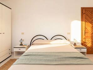 Ein Schlafzimmer mit einem Bett, Nachttischen, einer Lampe, einem Buch, einer Holztür und einem Kleiderschrank.
