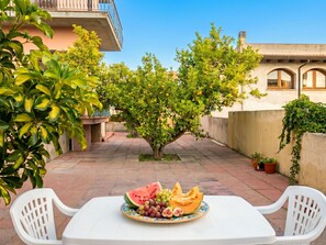 Eine Terrasse im Freien mit Esstisch, umgeben von Pflanzen und Gebäuden.