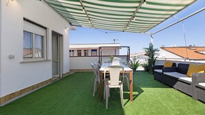 Un patio con césped artificial, una mesa con sillas, un sofá y un toldo a rayas.