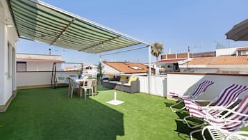 En tagterrasse med kunstgræs, et bord med stole, en sofa og stribede liggestole.