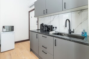 Eine kompakte Küche mit grauen Schränken, einer eingebauten Mikrowelle, einer Kaffeemaschine und einem Spülbecken mit Armatur.