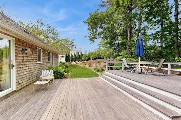 Eine Holzterrasse mit Gartenmöbeln, ein Rasen und ein Haus mit weißer Fassade.