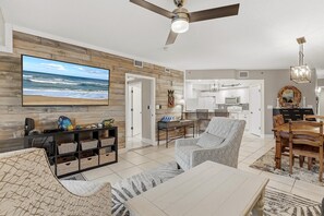 Ein modernes Wohnzimmer mit großem Fernseher, Holzpaneelen, einem Deckenventilator und einem Essbereich mit Holztisch und Stühlen.