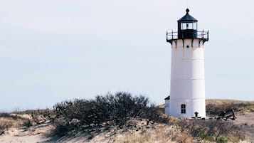 Un phare à l’extérieur blanc et au sommet noir, situé sur une dune de sable où la végétation est clairsemée.
