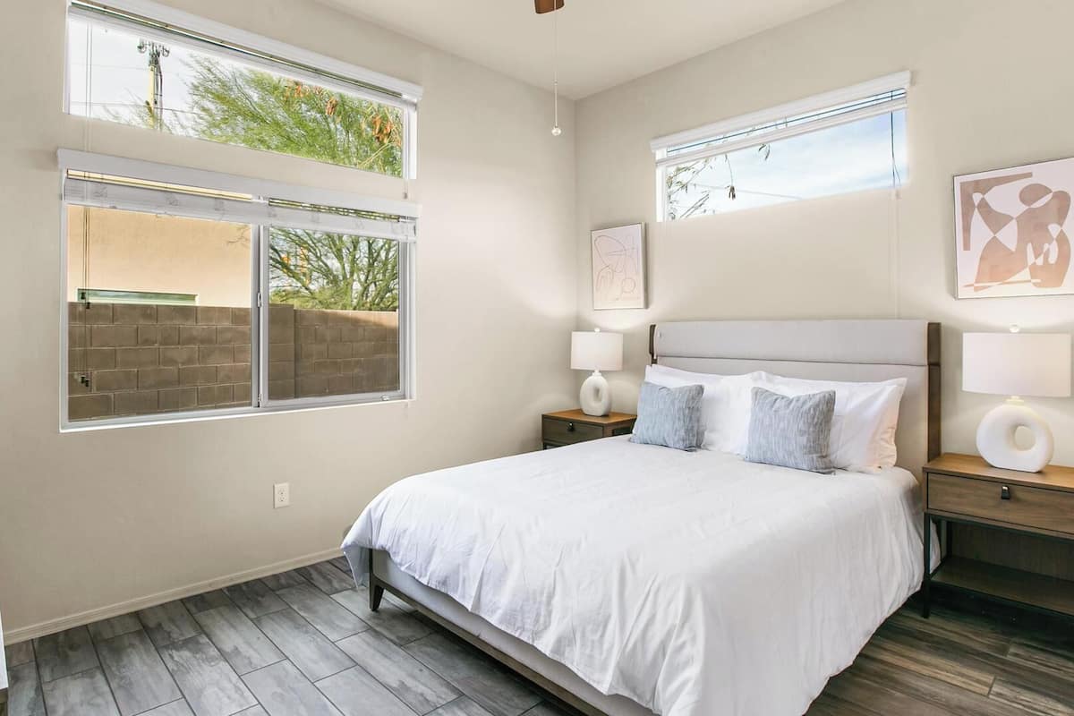 A bedroom with a bed, two bedside tables, a window, and artwork on the walls.